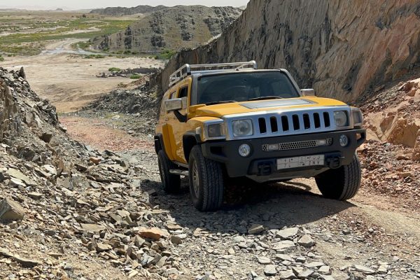 A yellow SUV navigating a rugged, rocky off-road terrain under a bright sky.