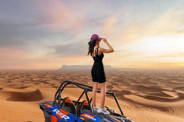 A woman stands confidently on an ATV amidst the vast sand dunes of Abu Dhabi, embracing adventure.