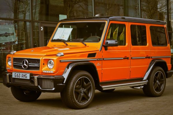 Bright orange Mercedes-Benz G Wagon parked in front of a building, showcasing luxury and style.