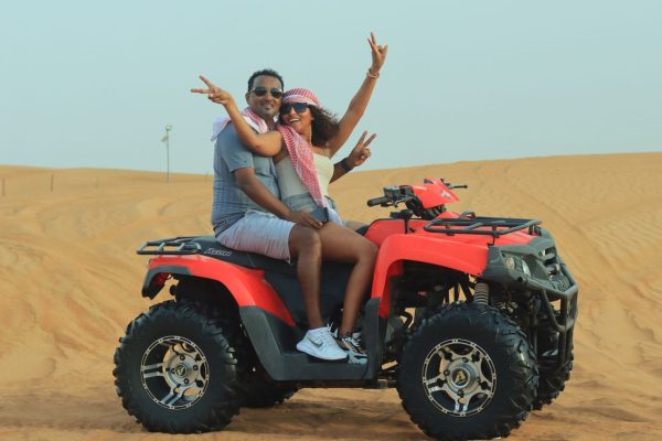 A happy couple enjoys an adventurous quad bike ride in the scenic Dubai desert during the day.