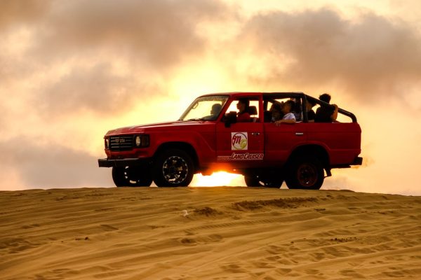 Red SUV driving over sand dunes at sunset, showcasing an adventurous off-road experience.